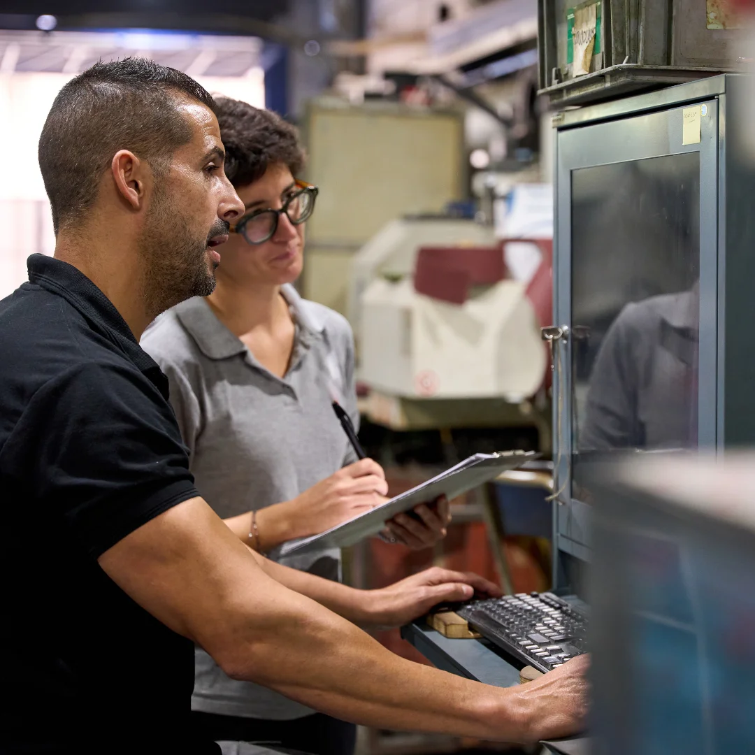 Manufacturing workers programming industrial machinery using computer in factory