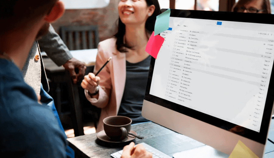Businessman working on mac with his emails on screen while co workers talk in background