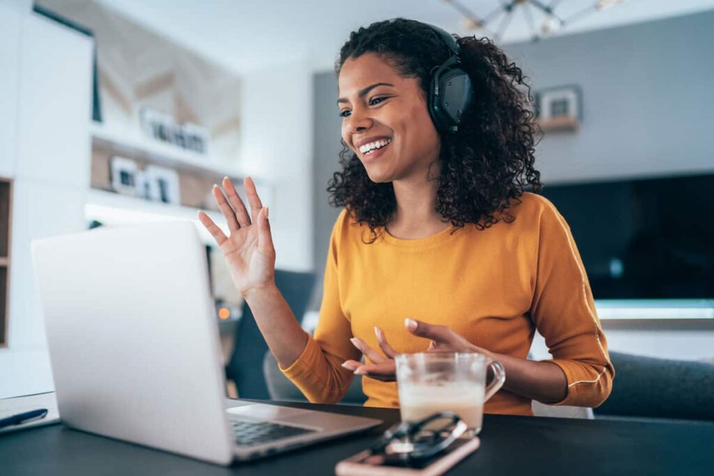woman working from home on call waving at laptop camera