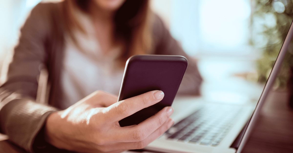 Woman holding her phone working on laptop